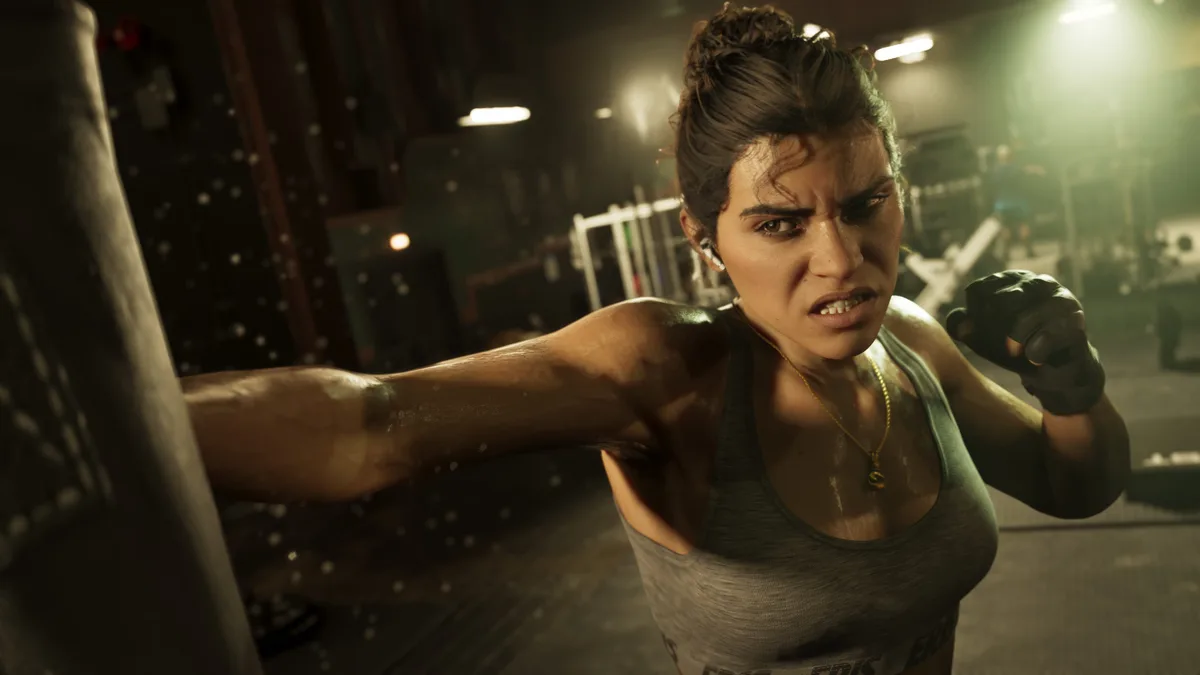 Lucia throwing a punch at a heavy bag in a dim gym, wearing a grey vest and gloves, in a Rockstar Games screenshot for GTA 6