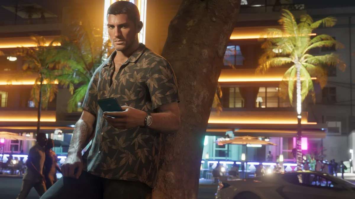Jason in a patterned shirt checks his phone on a neon lit street lined with palm trees at night in a Rockstar Games screenshot for GTA 6