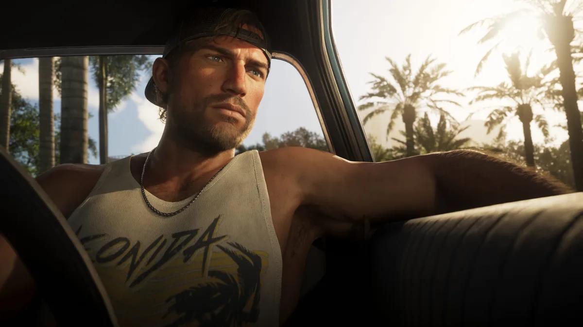 Jason in a backwards cap and Leonida vest sitting behind the wheel of a car with sunlit palm trees outside in a Rockstar Games screenshot for GTA 6