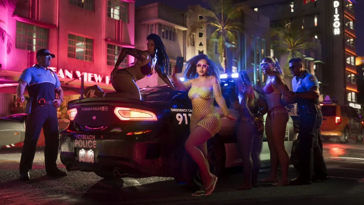 two Vice Beach Police officers beside a patrol car as women in swimwear pose on it outside a neon lit Vice City hotel at night in a Rockstar Games screenshot for GTA 6