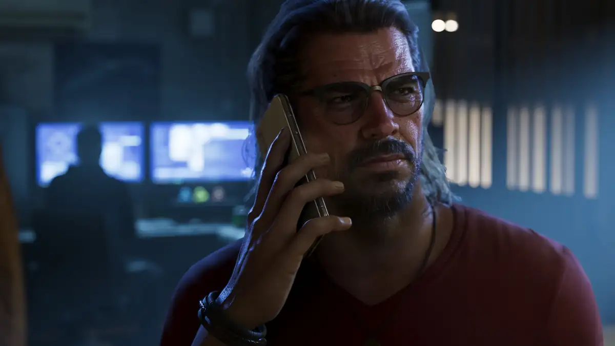 Raul Bautista talking on a phone in a dark room with computer screens behind him in a Rockstar Games image for GTA 6